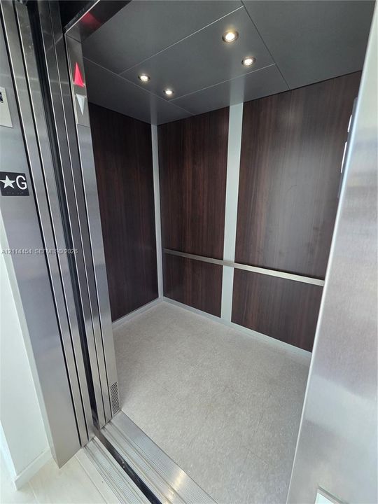 Private elevator featuring stainless steel door frames, rich wood-finish wall paneling, integrated recessed ceiling lighting, and a horizontal metal handrail