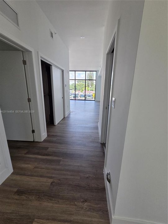 Hallway featuring wood-finish flooring, white walls, and floor-to-ceiling windows with dark framing