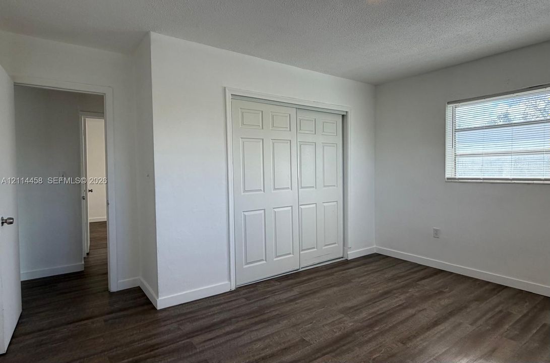Room featuring wood-finish flooring, white walls, a dual-panel sliding closet, and a window with horizontal blinds