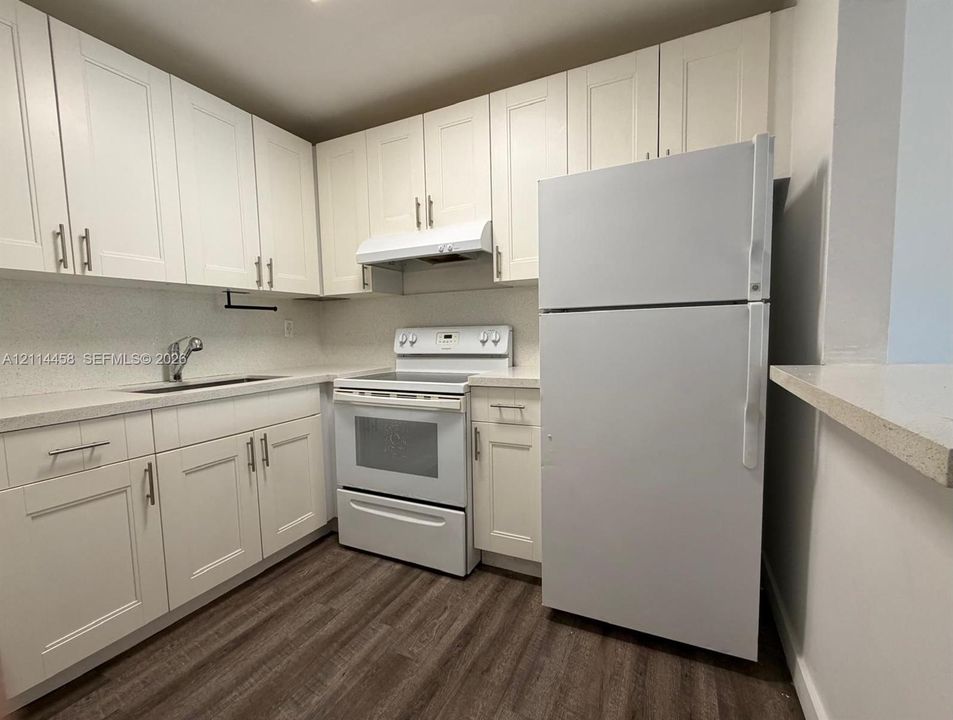 Kitchen featuring white shaker-style cabinetry, solid-surface countertops, wood-finish flooring, and white appliances including a top-freezer refrigerator and range