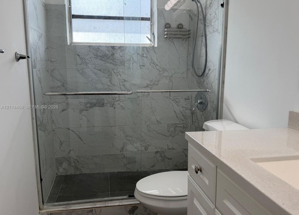 Walk-in shower with floor-to-ceiling veined tile surrounds and glass enclosure, vanity featuring a light-toned solid surface countertop, and integrated sink