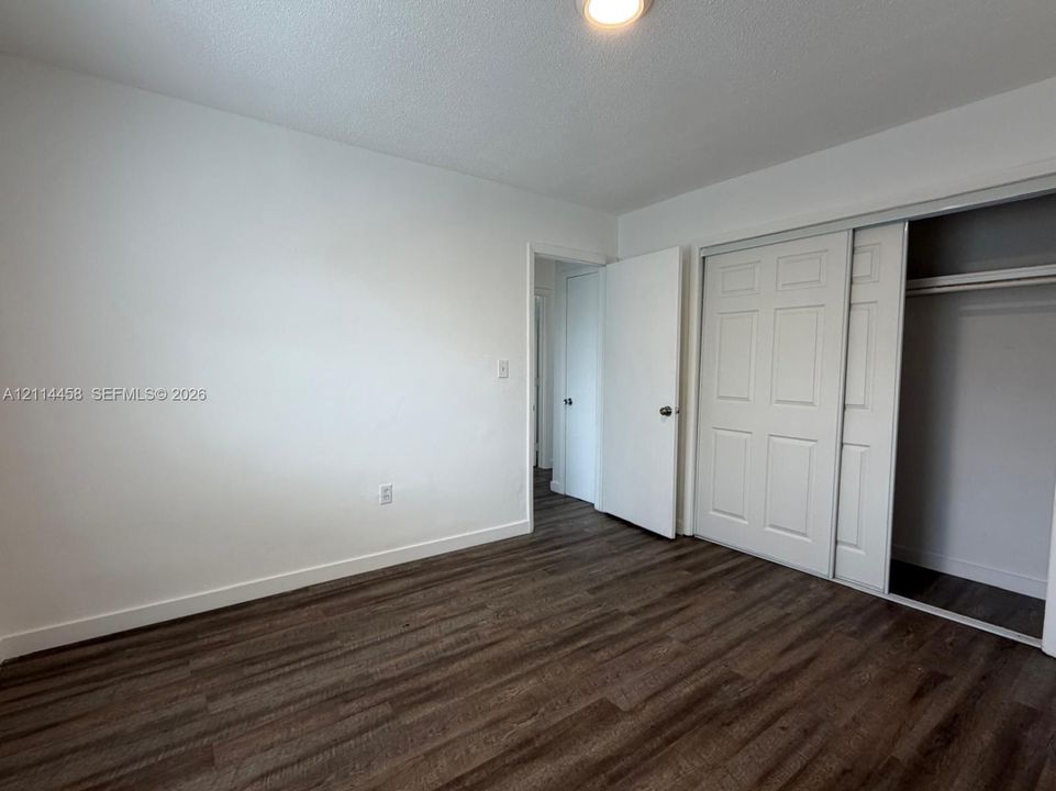Room featuring wood-finish flooring, white walls, and a closet with six-panel sliding doors