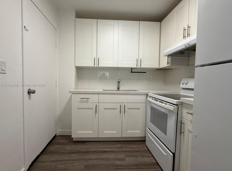 Kitchen featuring shaker-style cabinetry, solid-surface countertops, wood-finish flooring, and a stainless steel sink with a mounted faucet