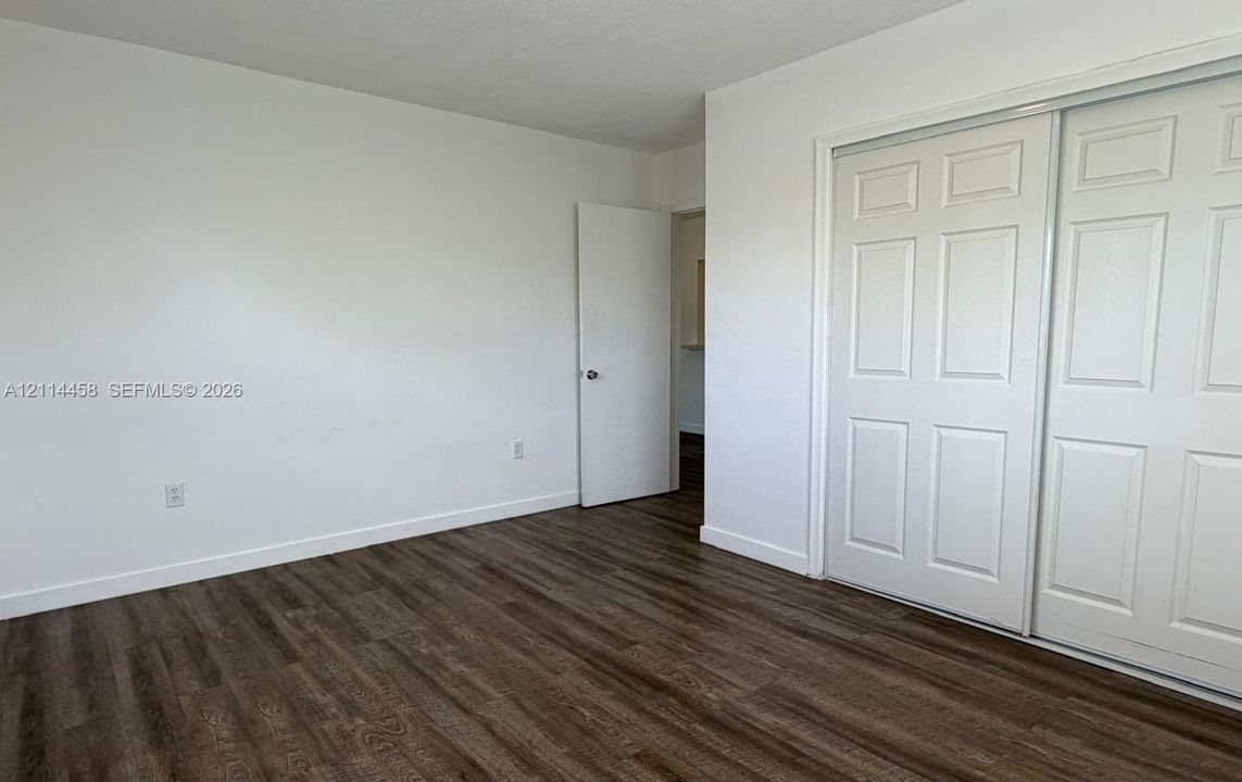 Room featuring wood-finish flooring, white walls, and a multi-panel sliding door closet