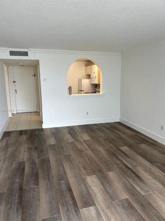 Interior featuring wood-finish flooring, a distinctive arched wall opening, crown molding, and tiled entryway flooring