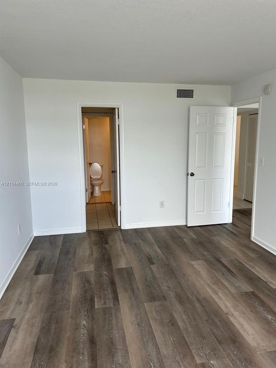 Neutral-toned interior space featuring wood-finish flooring, six-panel interior doors, and tile flooring in the secondary area