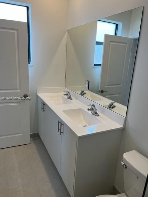 Double-sink vanity featuring a solid-surface countertop, white cabinetry with brushed-metal pulls, and a full-width wall mirror