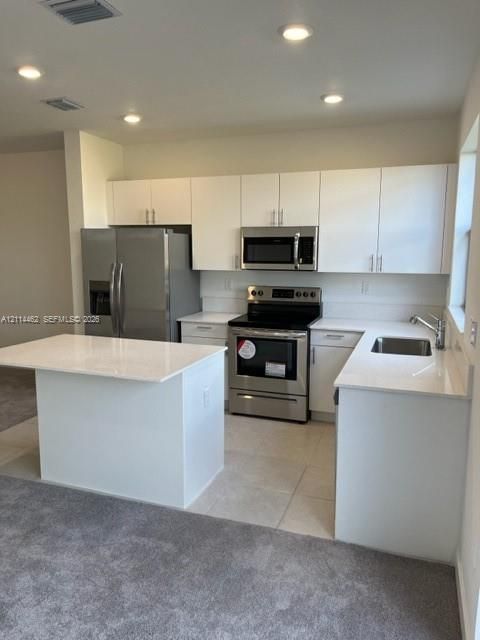 Kitchen featuring white flat-panel cabinetry, light-toned stone countertops, a central island, stainless steel appliances, and recessed ceiling lighting