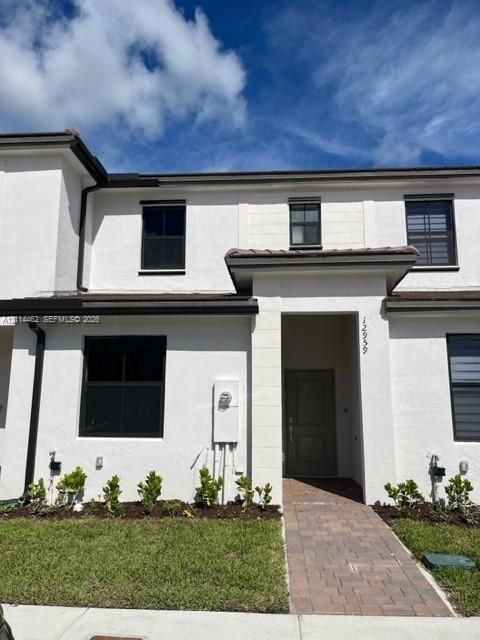 Exterior facade featuring a white stucco finish, dark-framed windows, a covered recessed entryway, and a paved walkway