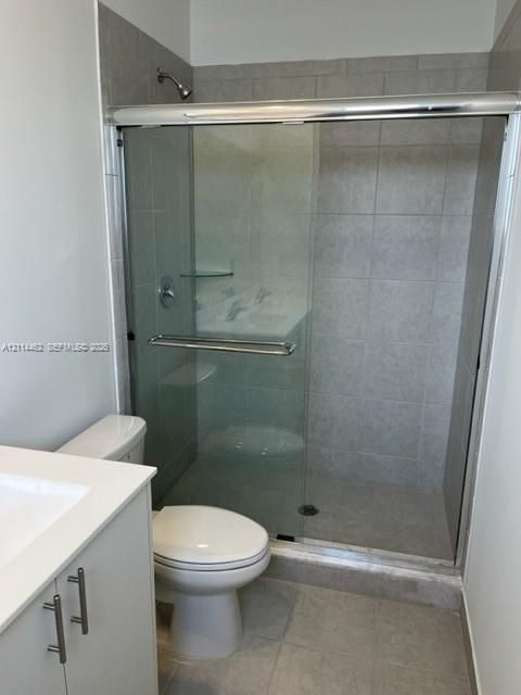Walk-in shower featuring a sliding glass enclosure, light-toned wall tile, and built-in corner shelving, accompanied by a white vanity with a rectangular sink and brushed metal hardware
