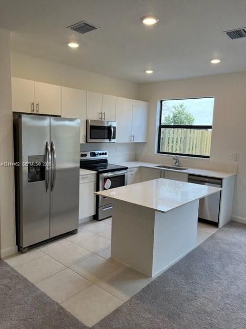 Kitchen featuring white cabinetry, solid-surface countertops, center island, stainless steel appliances, and tile flooring