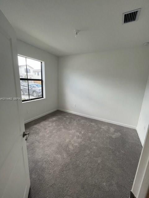 Neutral interior room featuring plush wall-to-wall carpeting, crisp off-white wall finishes, and a single-pane window with a black grid frame