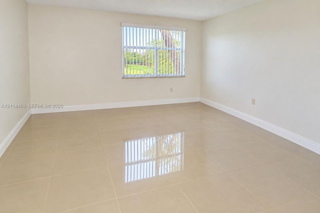 Neutral-toned interior space featuring polished large-format tile flooring, smooth wall finishes, and a single window with vertical blinds