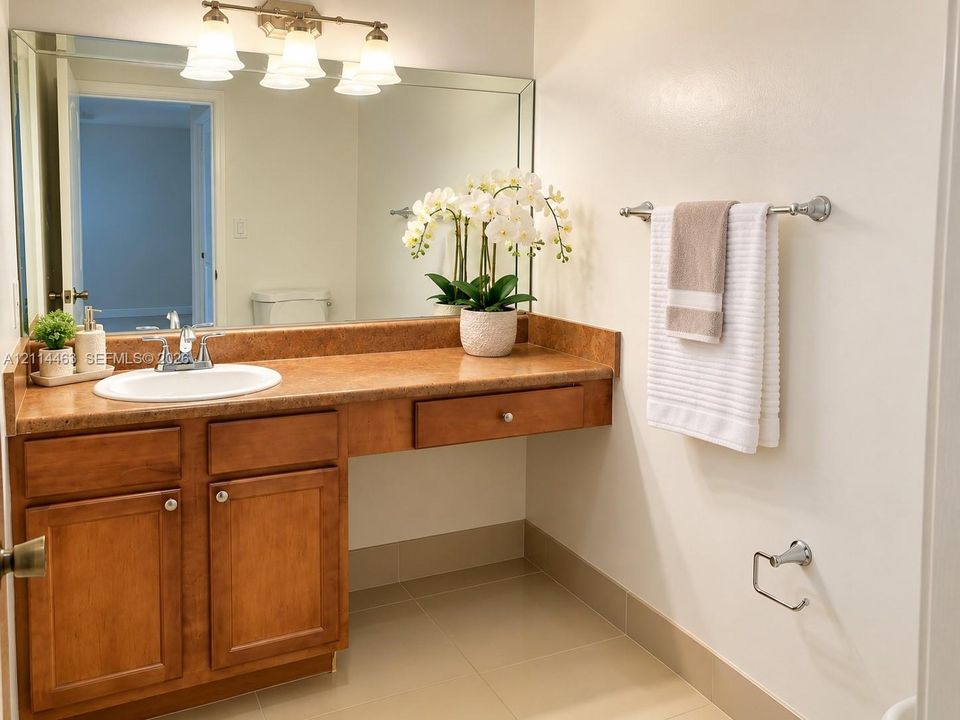Bathroom vanity featuring warm-toned cabinetry, an integrated stone-finish countertop with a circular drop-in sink, a large wall-mounted vanity mirror, a three-light fixture, and neutral tile flooring