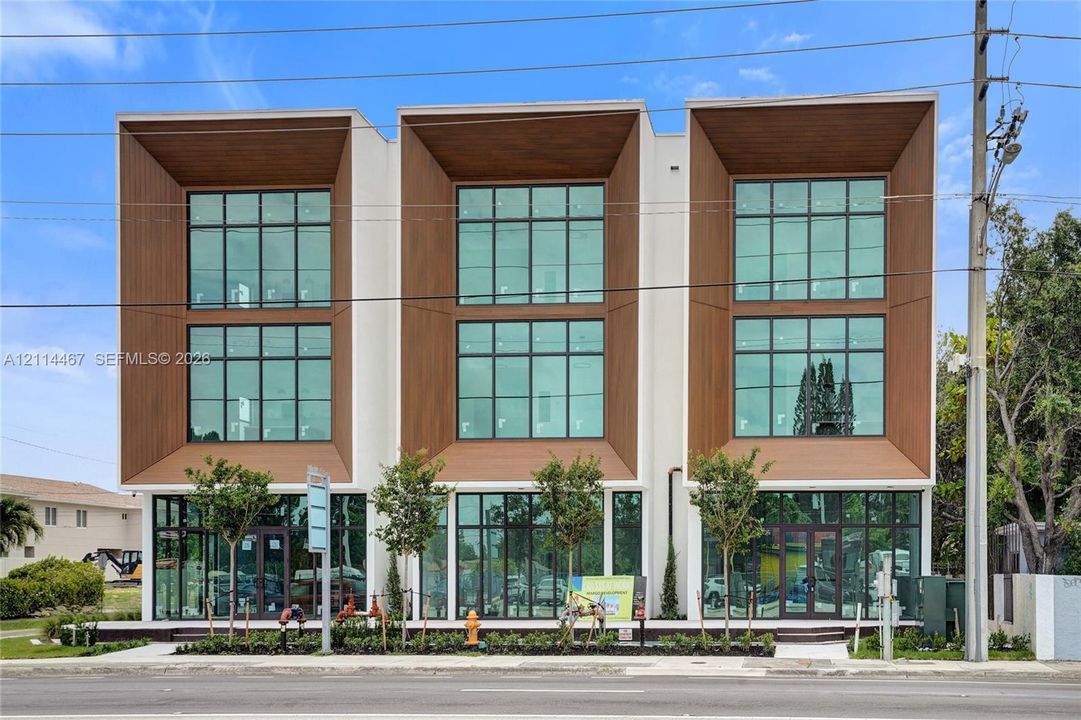 Modern three-story architectural exterior featuring smooth stucco finish, recessed wood-finish paneling, and expansive floor-to-ceiling glass windows