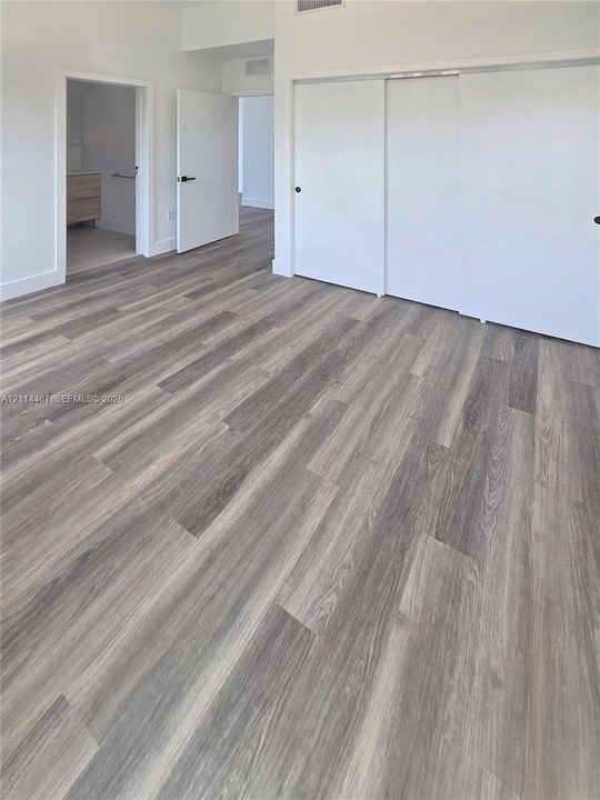 Interior room featuring wood-finish flooring, white walls, sliding closet doors, and solid-core passage doors