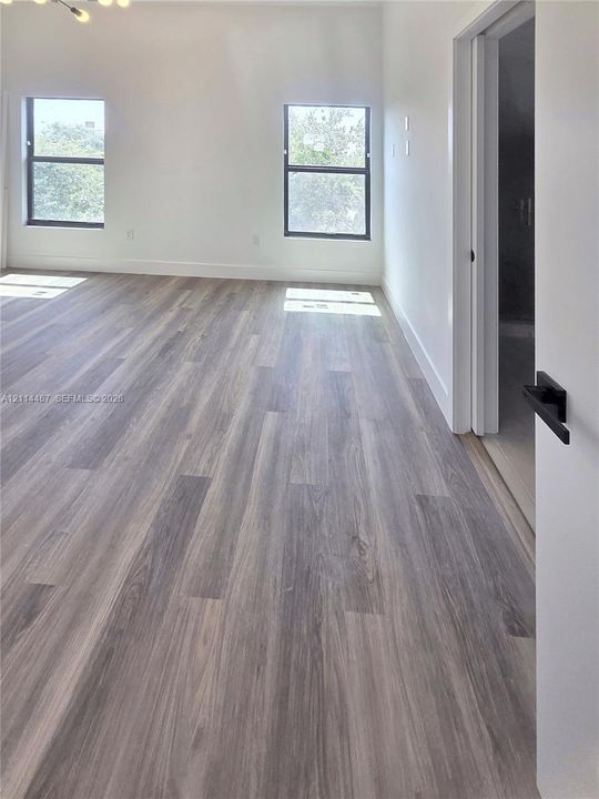 Neutral-toned wood-finish flooring, crisp white walls, dual windows with dark frames, and a modern door featuring matte black hardware