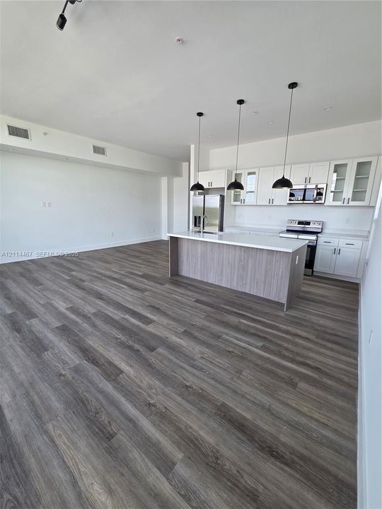 Kitchen featuring white cabinetry, wood-finish island with stone countertop, stainless steel appliances, and three pendant lights over wood-finish flooring