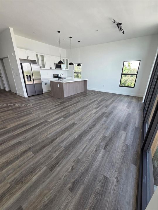 Kitchen featuring wood-finish flooring, white shaker cabinetry, a center island with countertop seating, stainless steel appliances, and pendant lighting