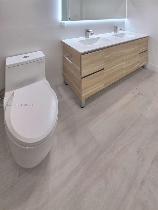 Double vanity with a light wood-finish cabinetry, rectangular integrated sinks, white countertop, and wide-format tile flooring