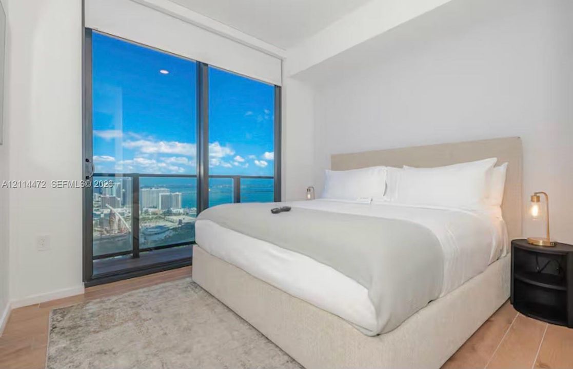 Floor-to-ceiling glass sliding doors, private balcony, wood-finish flooring, and expansive urban and water scenery
