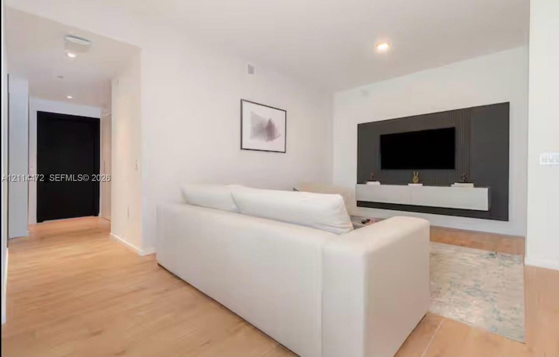 Living area featuring wood-finish flooring, a charcoal-toned paneled accent wall, a floating built-in console, and a solid black entry door