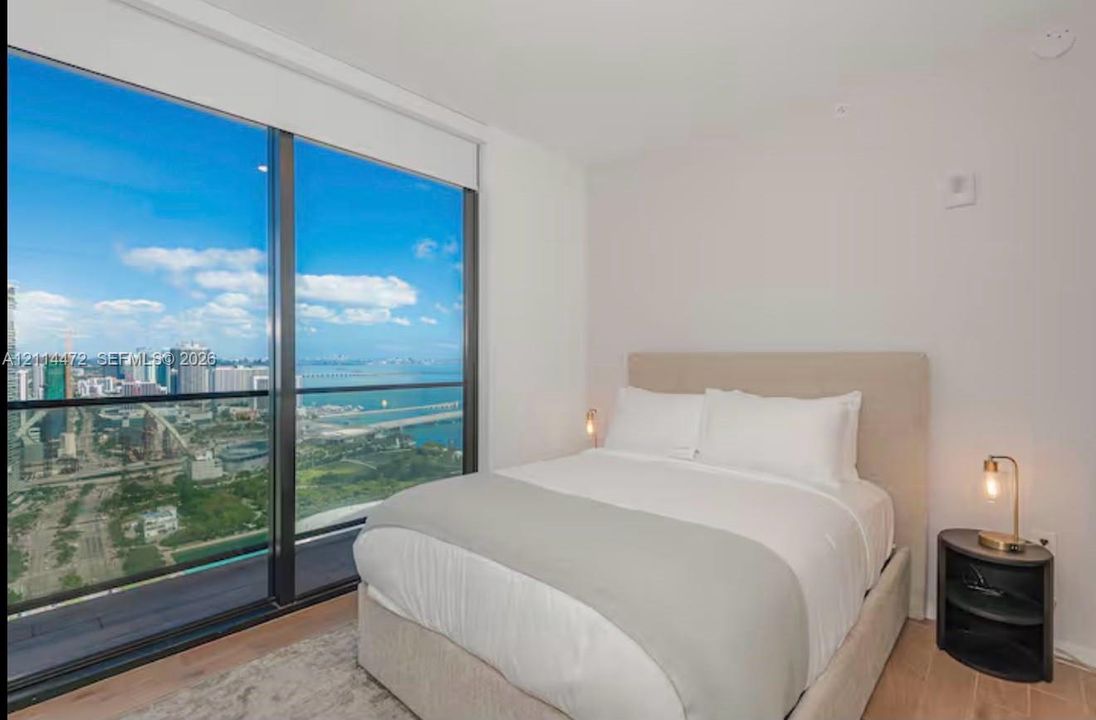 Floor-to-ceiling windows, wood-finish flooring, and expansive urban and water scenery