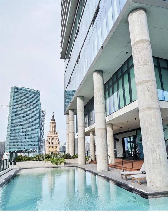 Outdoor swimming pool featuring a concrete deck, floor-to-ceiling glass building facade, and prominent structural columns