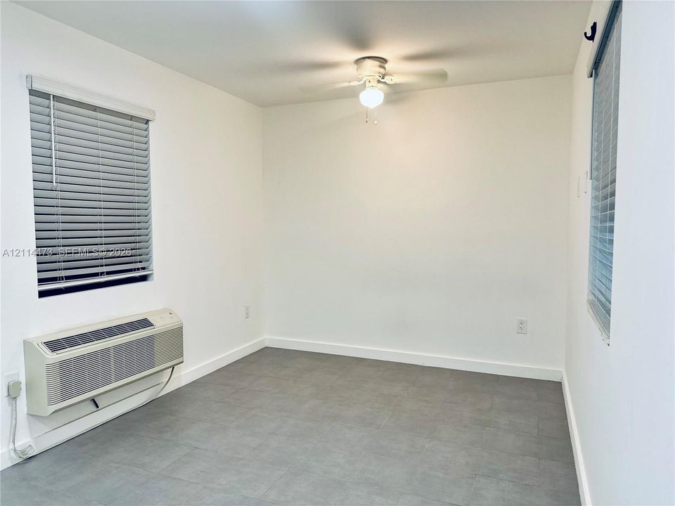 Neutral interior featuring gray tile flooring, white walls, dual windows with blinds, and a ceiling fan with light fixture