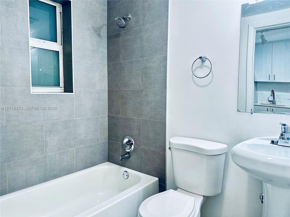 Bathroom featuring floor-to-ceiling large-format gray tile surround, white pedestal sink, chrome fixtures, and a glass-pane window