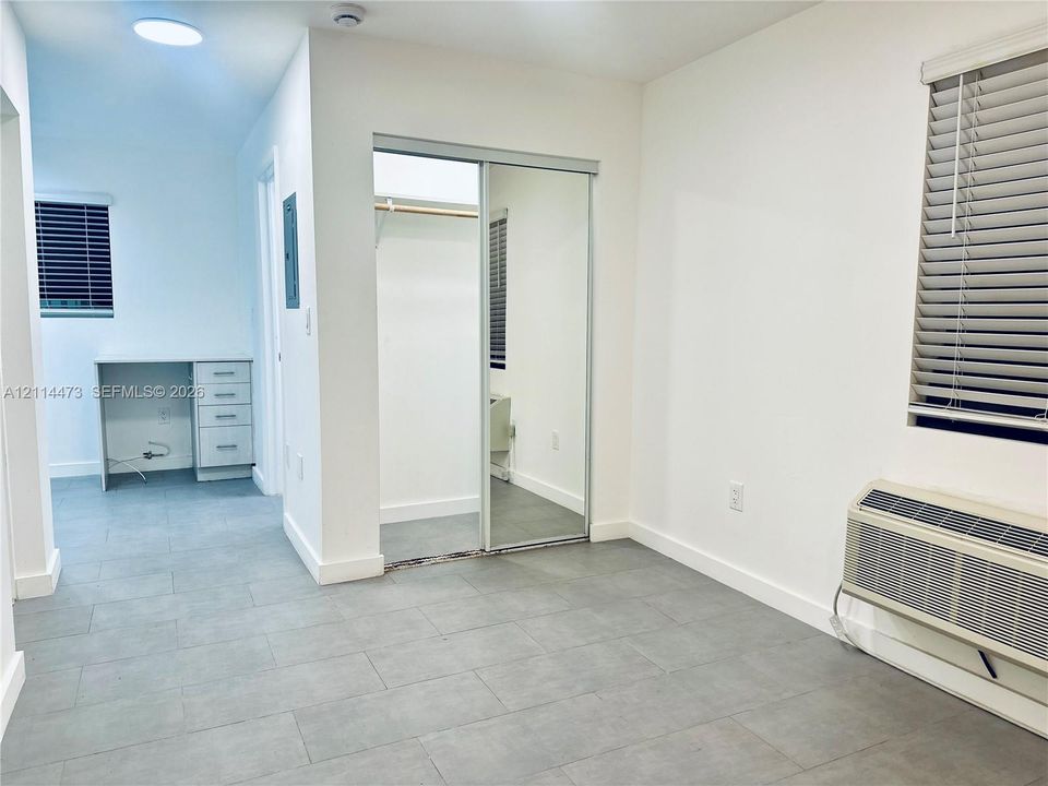 Neutral-toned tile flooring, built-in desk area with drawer storage, sliding mirrored closet doors, and window blinds
