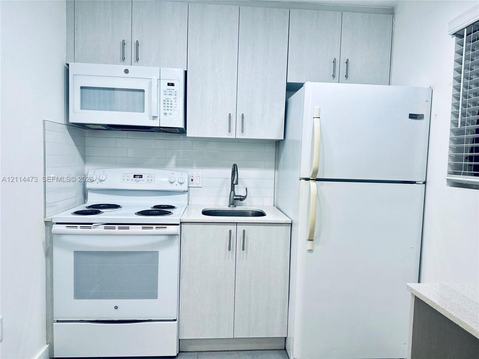 Kitchen featuring light-toned cabinetry, white subway tile backsplash, white electric range with over-the-range microwave, and a stainless steel sink with a high-arc faucet