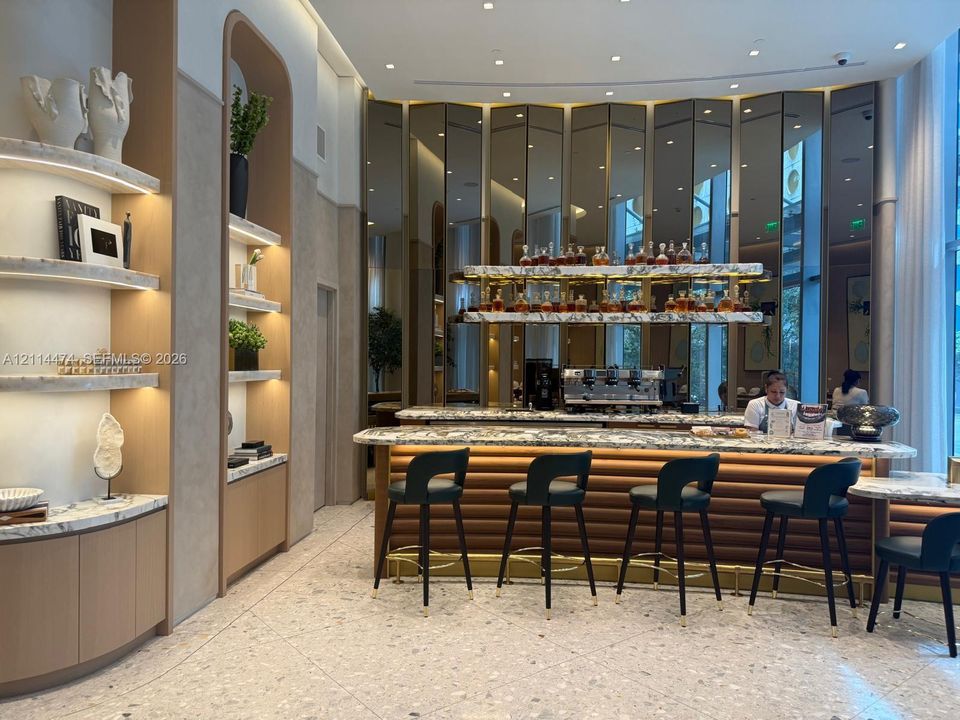 Bar area featuring a stone-topped counter, reeded wood-finish base, integrated lighting, stone shelving, and a mirrored paneled wall