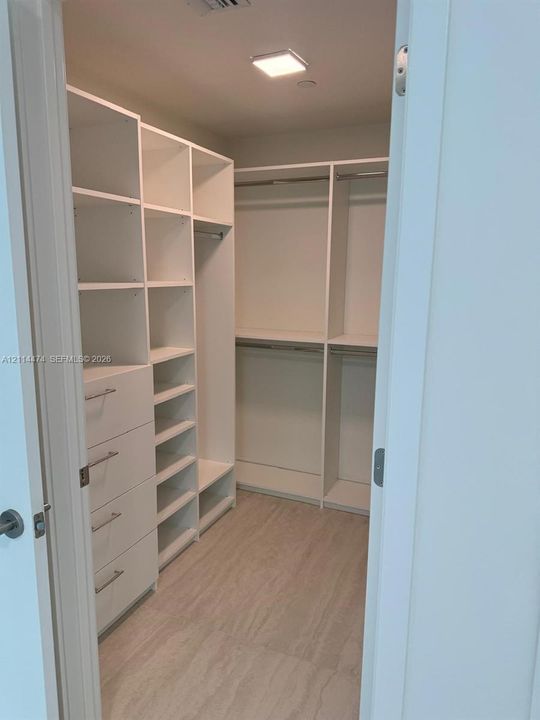Walk-in closet featuring white built-in shelving, integrated dresser drawers with metal hardware, double-tier hanging rods, and wood-finish flooring