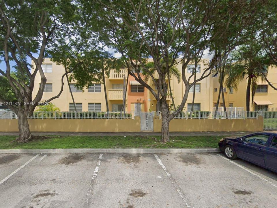 Multi-story building exterior featuring a stucco facade, integrated private balconies, and a perimeter security fence