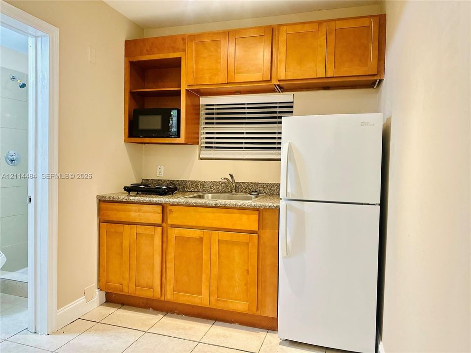 Kitchenette featuring natural wood cabinetry, stone-finish countertops, stainless steel sink with high-arc faucet, and tiled flooring