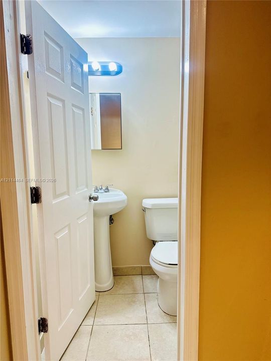 Restroom featuring a porcelain pedestal sink with a dual-handle faucet, a white two-piece toilet, ceramic tile flooring, and a wall-mounted mirrored medicine cabinet