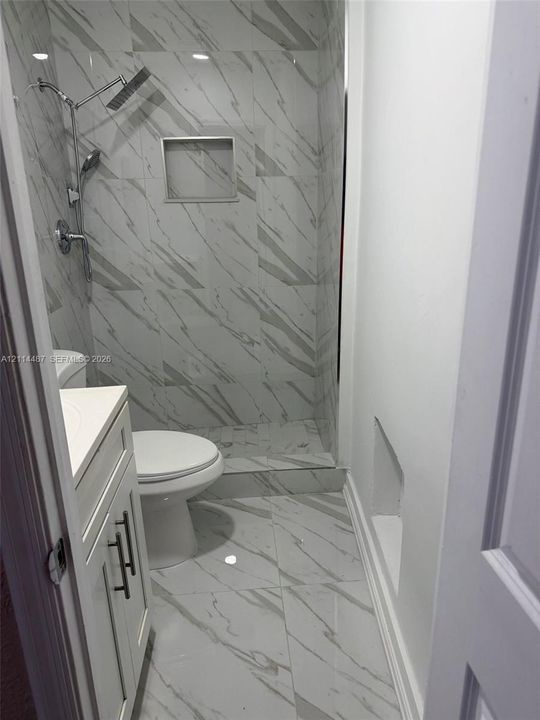 Walk-in shower featuring large-format tile with neutral veining, a built-in recessed shelf, a dual-head rainfall shower system, and vanity cabinetry with brushed metal hardware