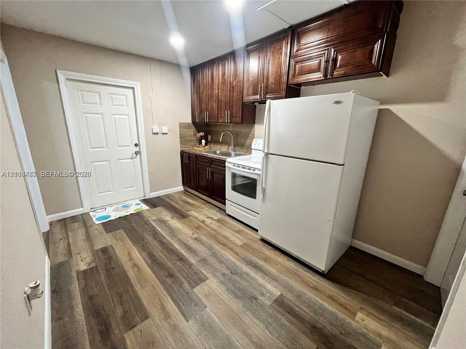 Kitchen featuring dark wood-finish cabinetry, wood-finish flooring, a stainless steel undermount sink with a gooseneck faucet, and a six-panel door