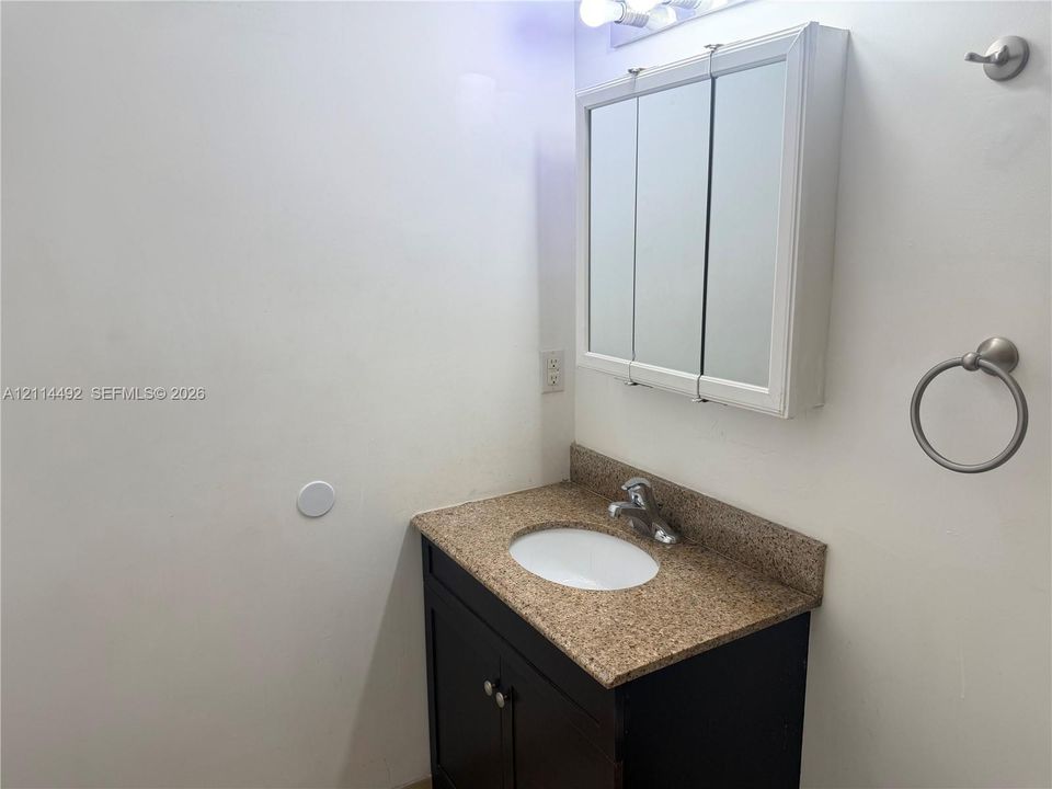 Bathroom vanity featuring a dark-finish base cabinet, stone-finish countertop with an integrated oval basin, metallic faucet, tri-fold mirrored medicine cabinet, and wall-mounted hardware