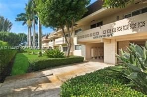 Multi-story exterior featuring patterned balcony screens, stone-paver walkways, manicured shrubbery, and mature palm trees