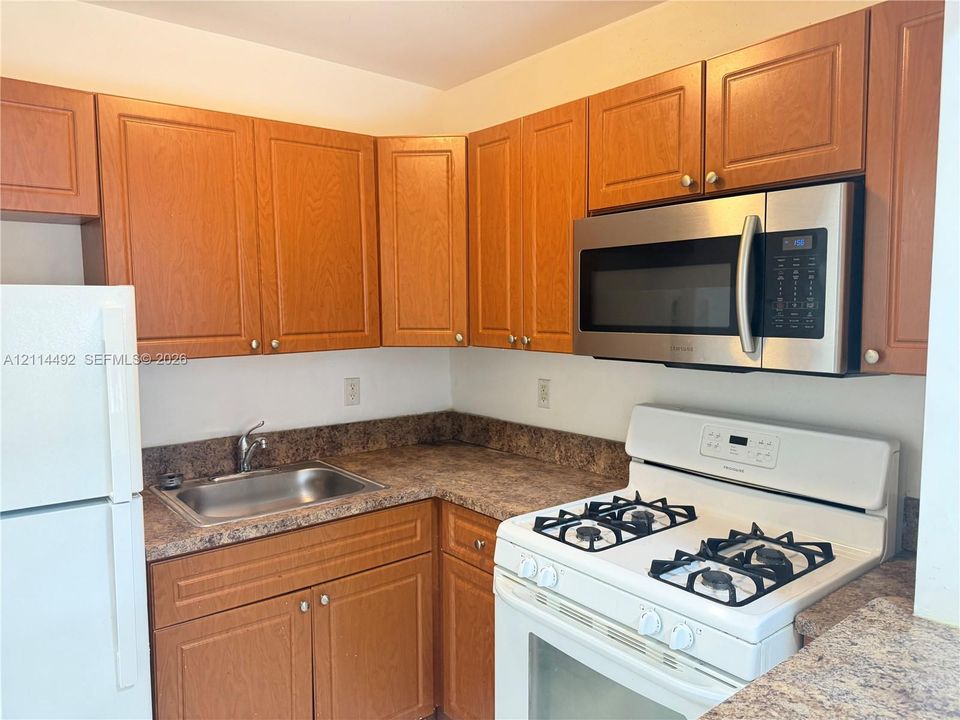 Kitchen featuring wood-finish cabinetry, stone-pattern laminate countertops, stainless steel sink, over-the-range microwave, and white gas range