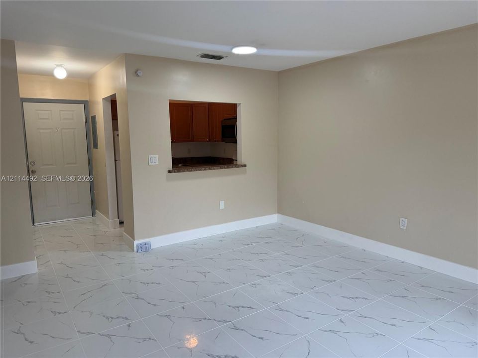 Open-concept living space featuring large-format tile flooring with a marble-finish pattern and a pass-through window to the kitchen