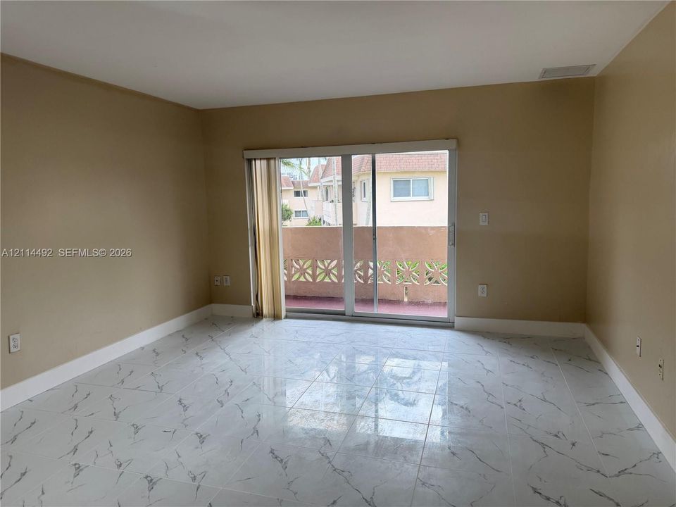 Large-format tile flooring with a neutral veined pattern and sliding glass doors leading to a private balcony with decorative concrete railing