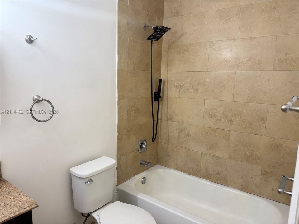 Bathtub with a large-format tile surround, square rainfall shower head with a secondary handheld sprayer, and polished chrome plumbing fixtures