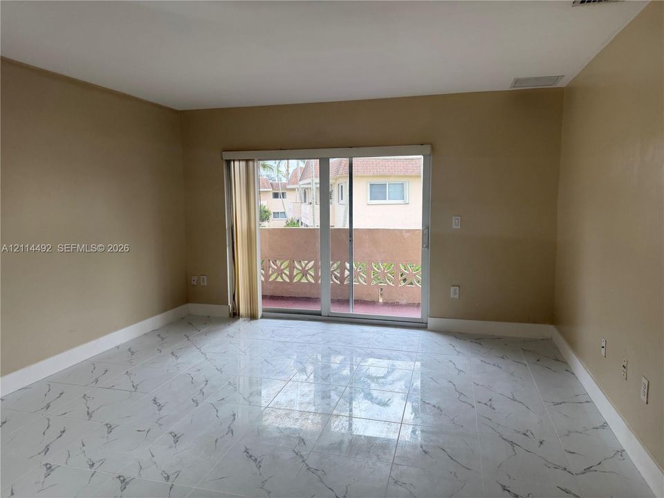 Interior space featuring large-format tile flooring with a veined pattern and sliding glass doors opening to a covered balcony with a decorative concrete screen