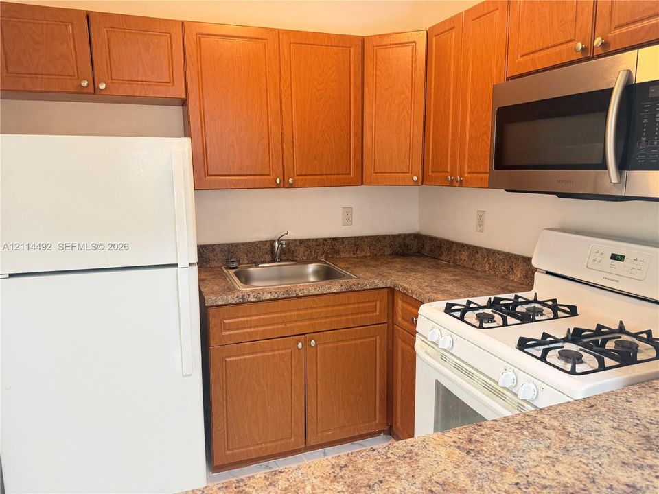 Kitchen featuring wood cabinetry, laminate countertops, a stainless steel sink with a chrome faucet, a gas range, and a built-in microwave