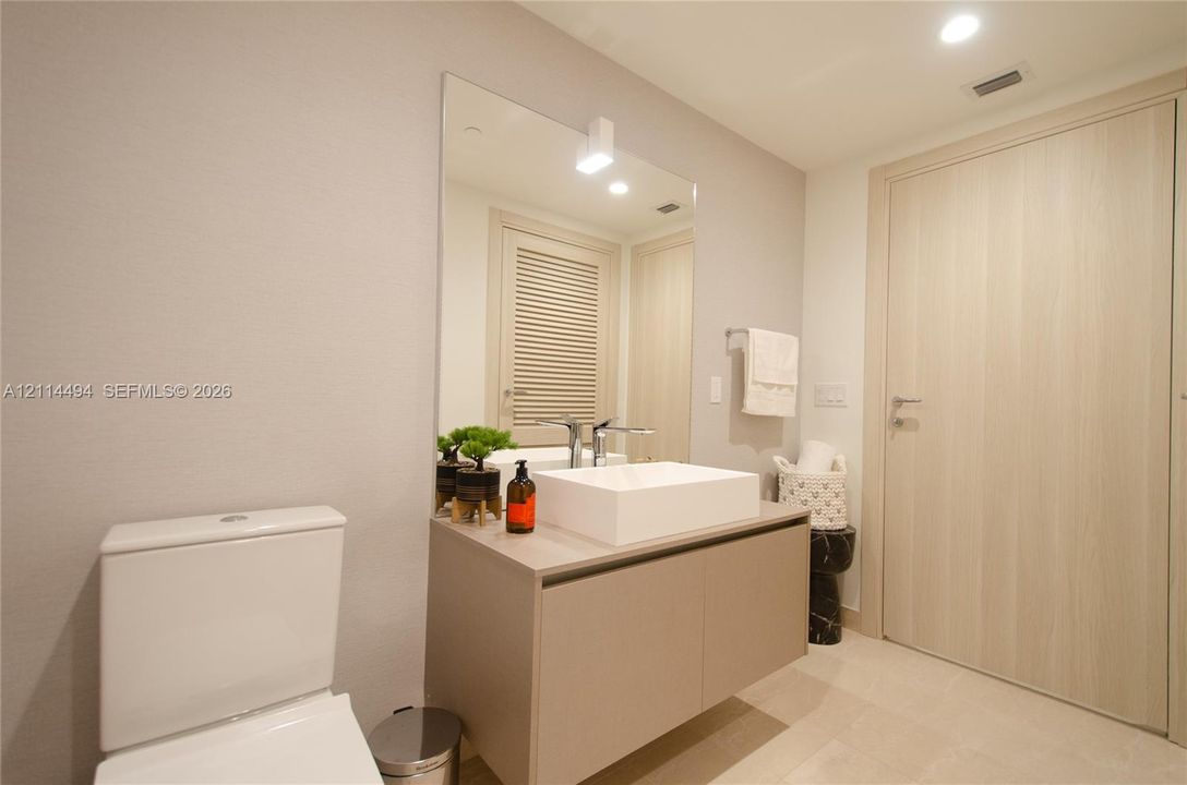 Floating vanity featuring a flat-panel cabinet, rectangular vessel sink, and chrome faucet, complemented by a large frameless wall mirror and wood-finish door