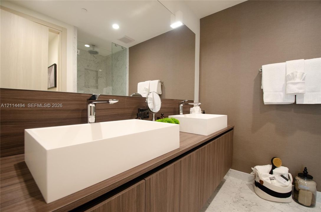 Floating wood-finish vanity with dual rectangular vessel sinks, polished chrome faucets, large frameless mirror, and walk-in shower with stone-finish surround