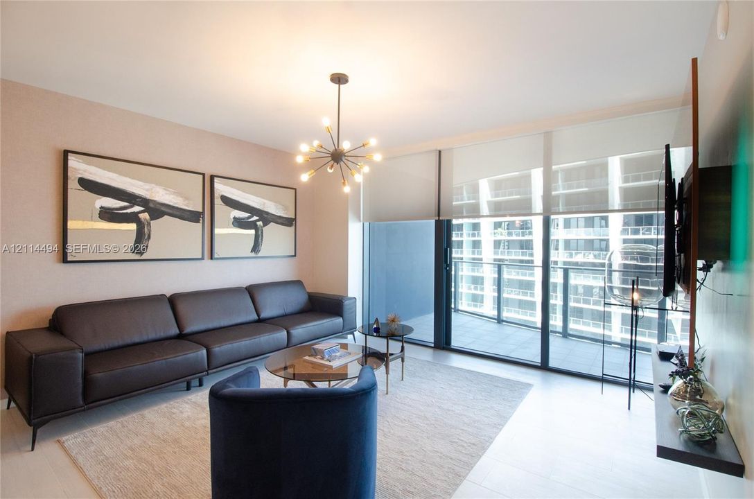 Floor-to-ceiling sliding glass doors, private balcony, contemporary multi-arm chandelier, and light-toned tile flooring